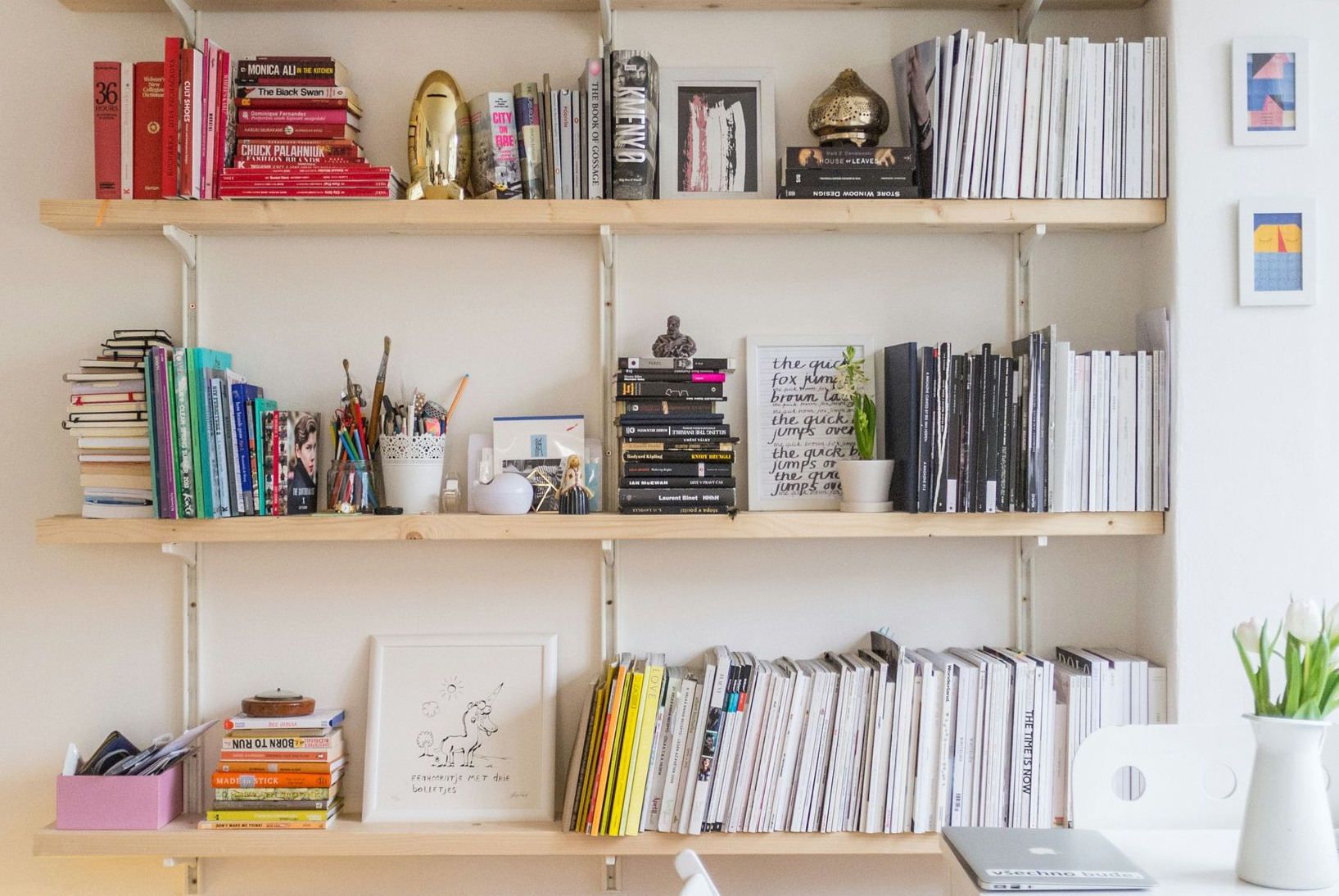 Wooden shelves filled with books, notebooks, pens, and craft supplies in a bright room