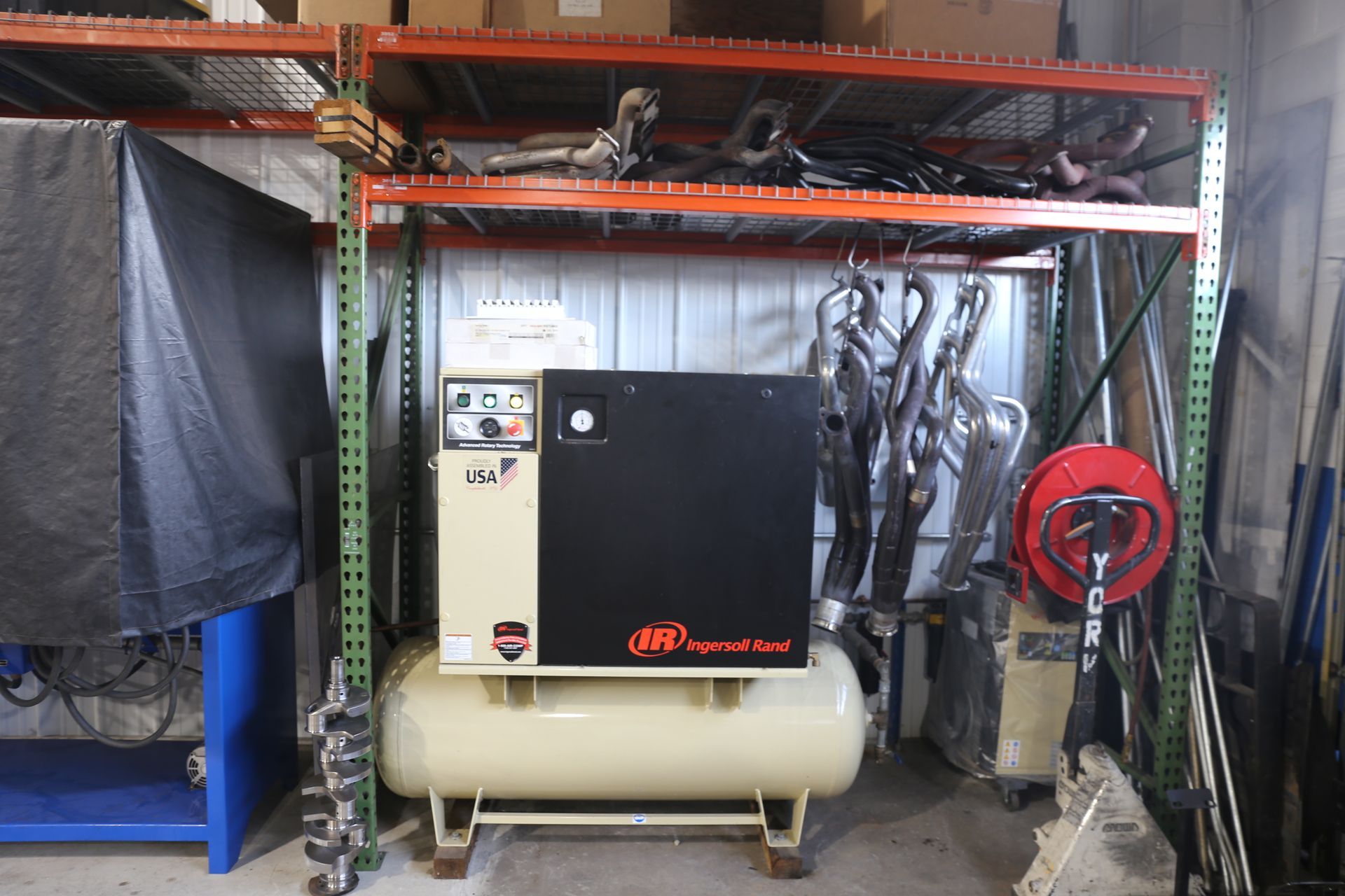 An air compressor with a beige tank and black cabinet inside a storage rack.
