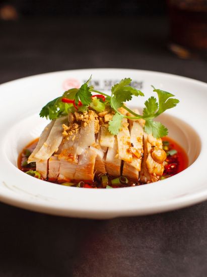 Sliced roasted meat garnished with cilantro on a white plate in red sauce