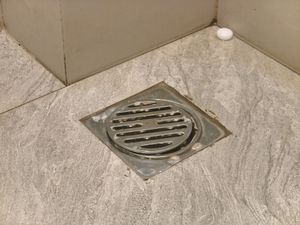 Floor drain with metal grate in a tiled shower corner.