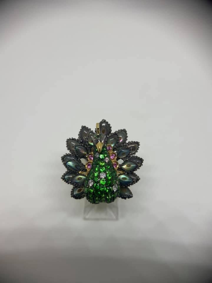 Jeweled green and black floral brooch on a clear stand against a gray background