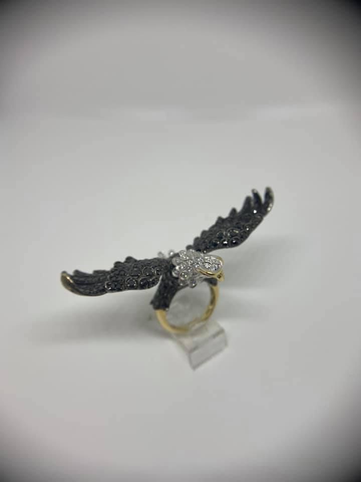 Black winged ring with a gold band displayed on a white surface