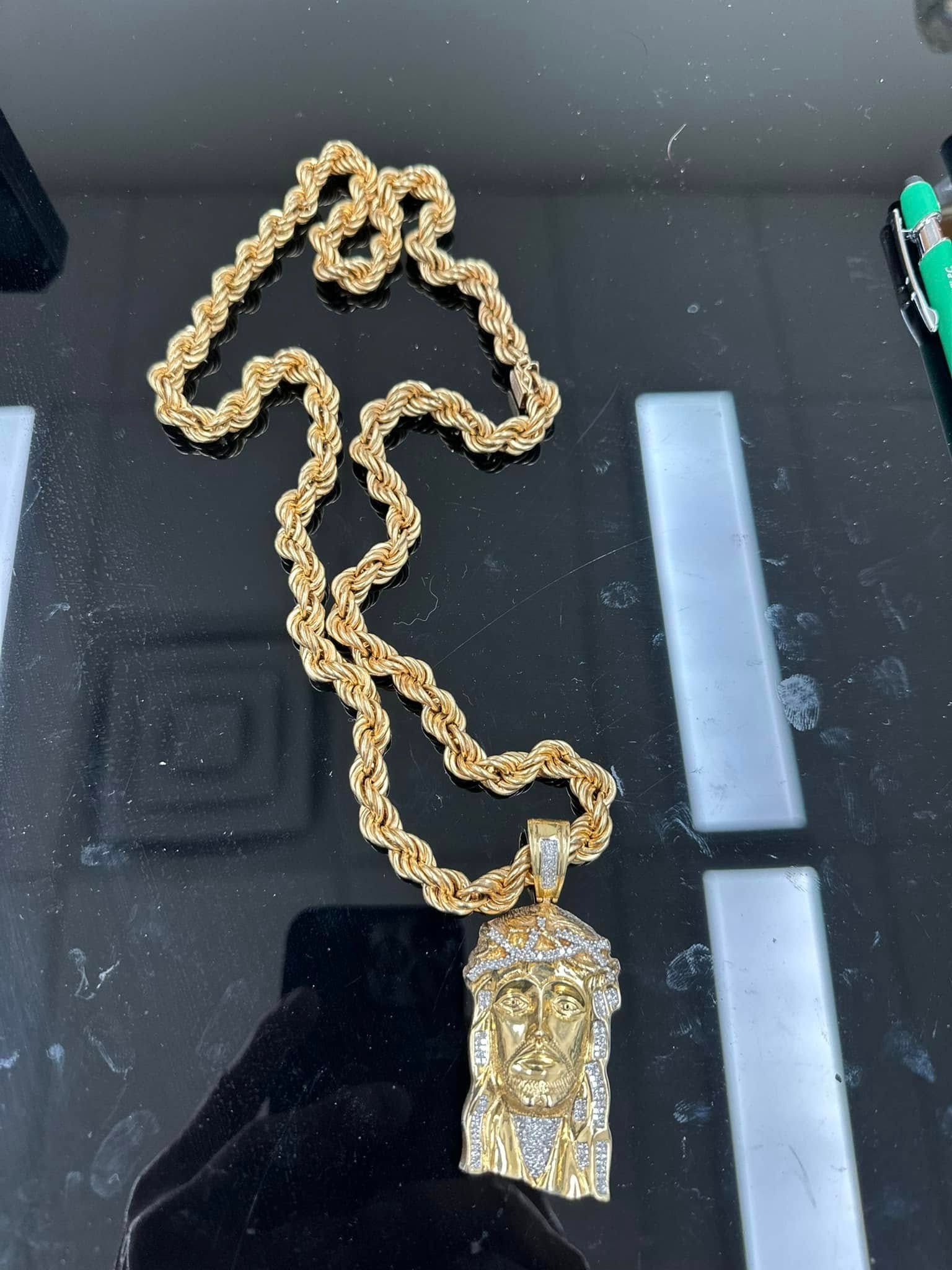 Gold chain necklace with a rectangular pendant on a black reflective surface
