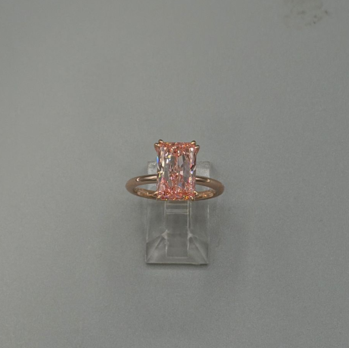 Tiny pink crystal ring on a clear square stand against a plain gray background