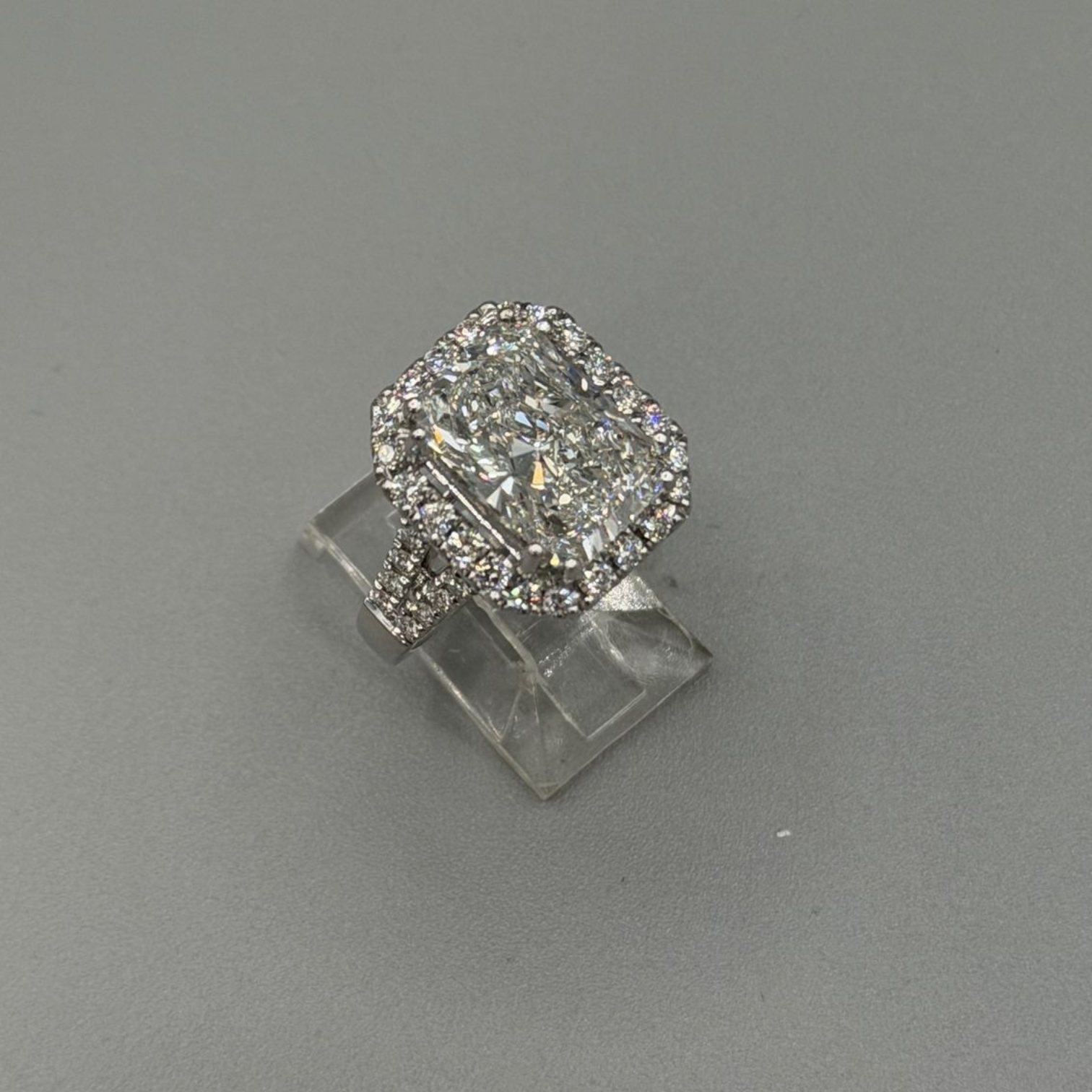 Diamond halo ring on a clear stand against a gray background