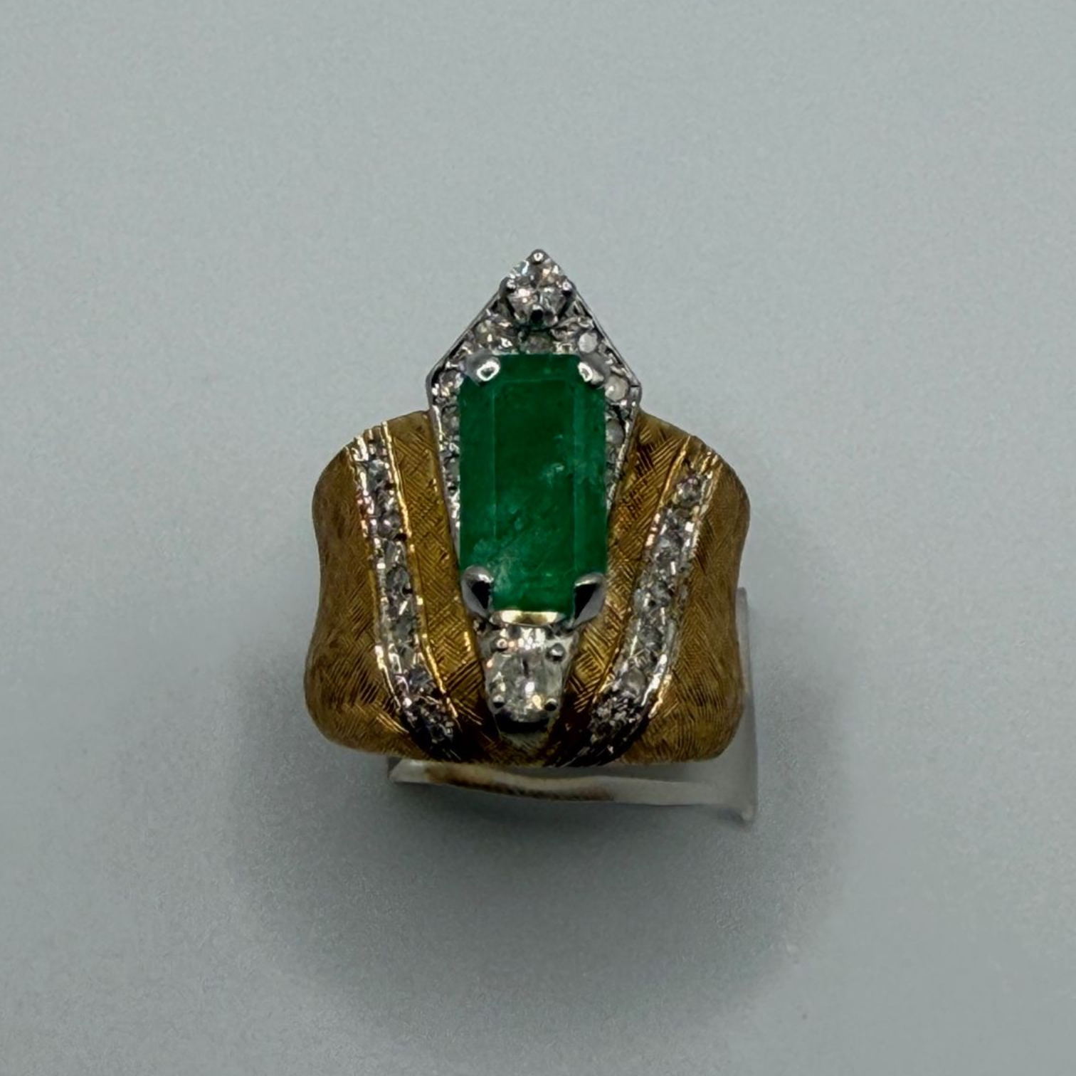 Gold ring with green rectangular gemstone and silver accent stones on a plain background