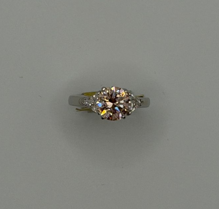A silver ring with a round, sparkling multicolor gemstone on a plain gray background