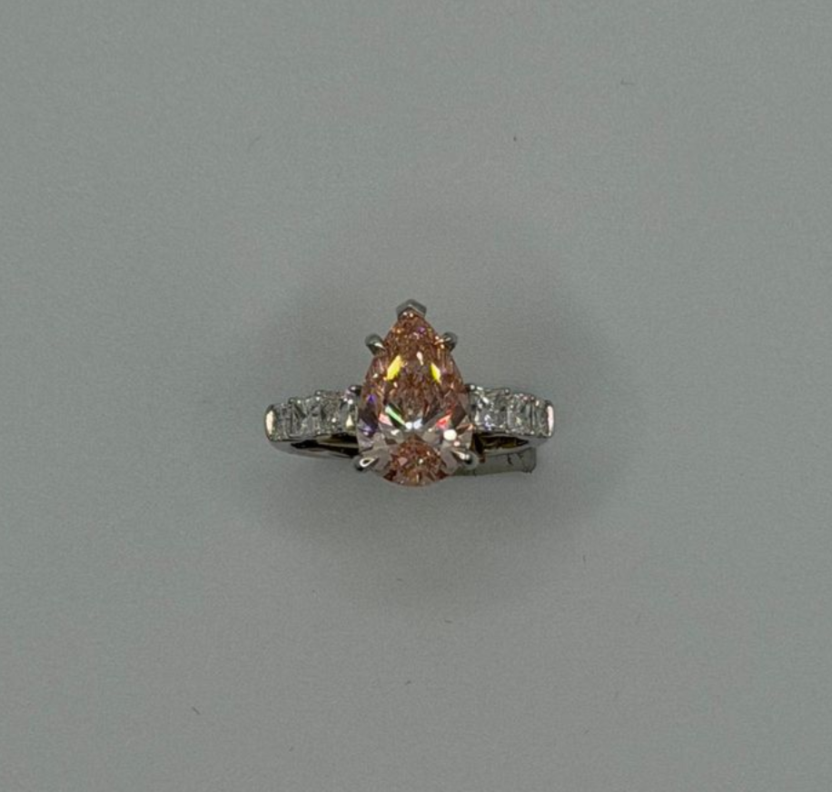 A pear-shaped pink gemstone ring with small side stones on a plain gray background