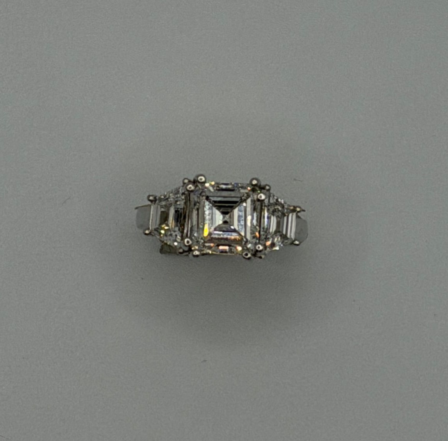 Silver ring with a rectangular clear gemstone and side stones on a gray background