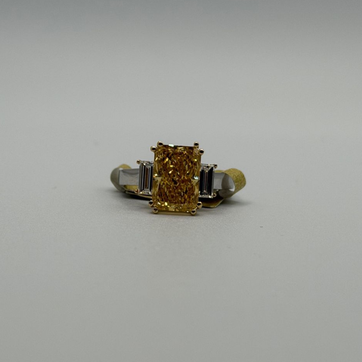 Gold and silver ring with a rectangular yellow gemstone on a plain gray background