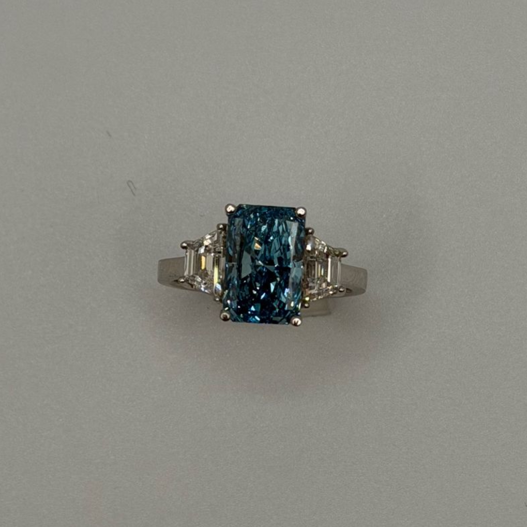 Silver ring with a rectangular blue gemstone and small side stones on a plain gray background