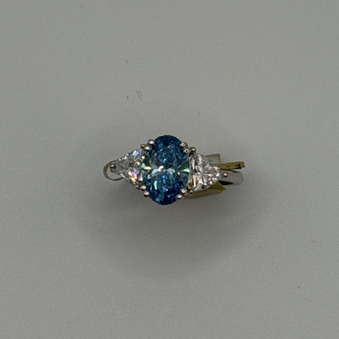 Silver ring with a blue oval gemstone and clear side stones on a light gray background