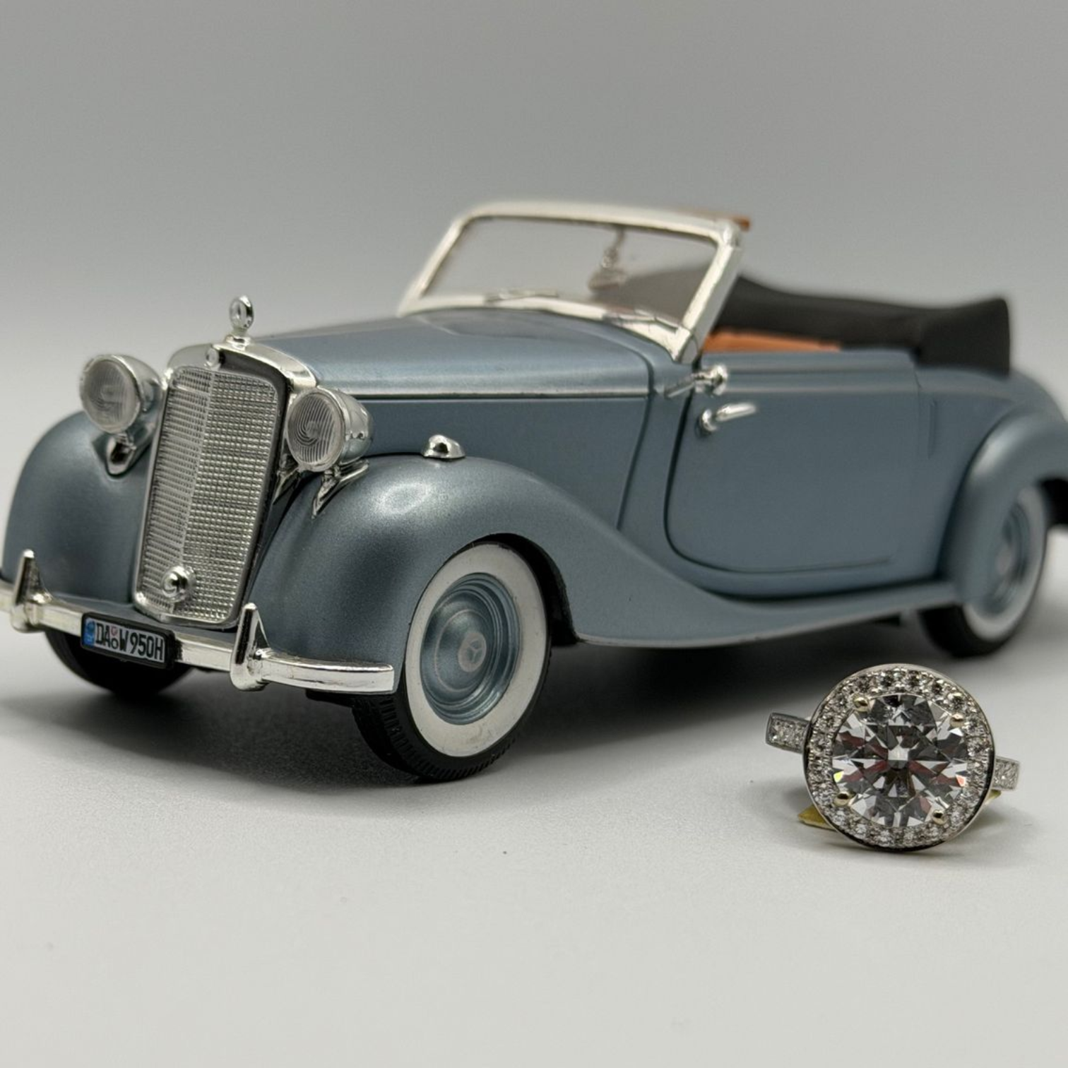 Blue vintage convertible model car beside a large diamond ring on a gray background