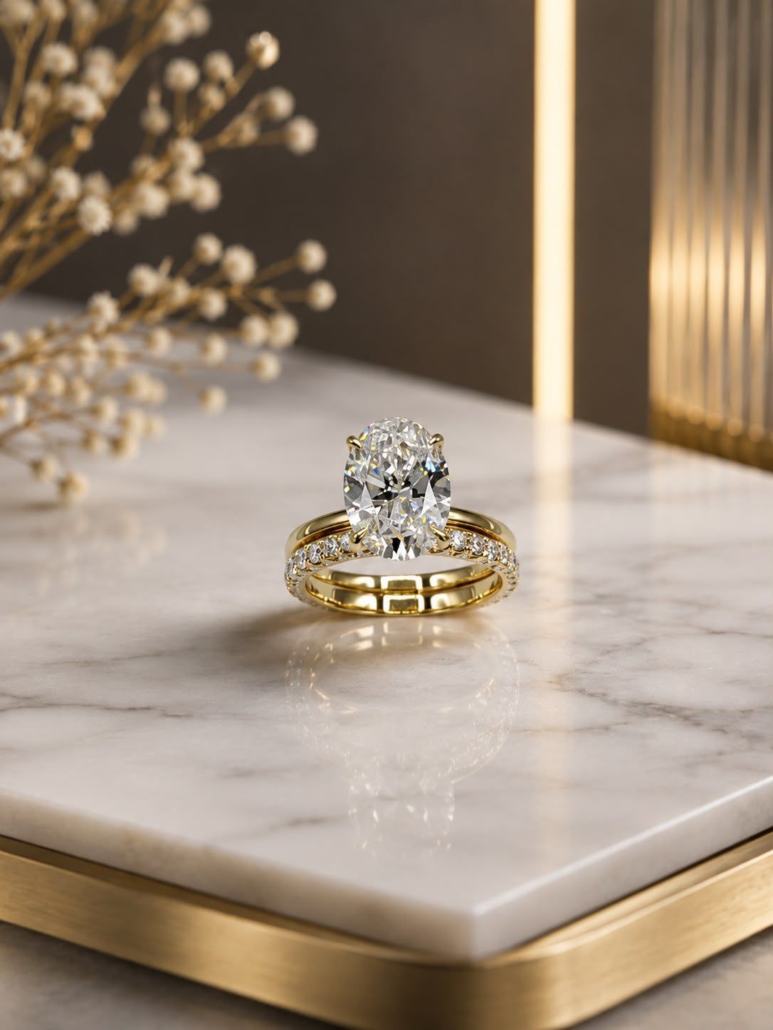Gold wedding rings with a diamond on a white marble display, lit warmly with decorative branches nearby