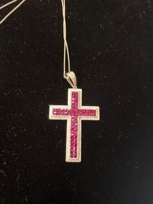 Pink cross pendant hanging on a thin cord against a dark background
