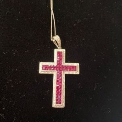 Pink gemstone cross pendant on a silver chain against a black background