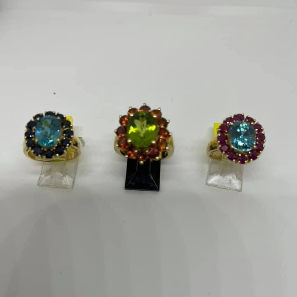Three colorful jeweled rings displayed on clear stands against a white background.