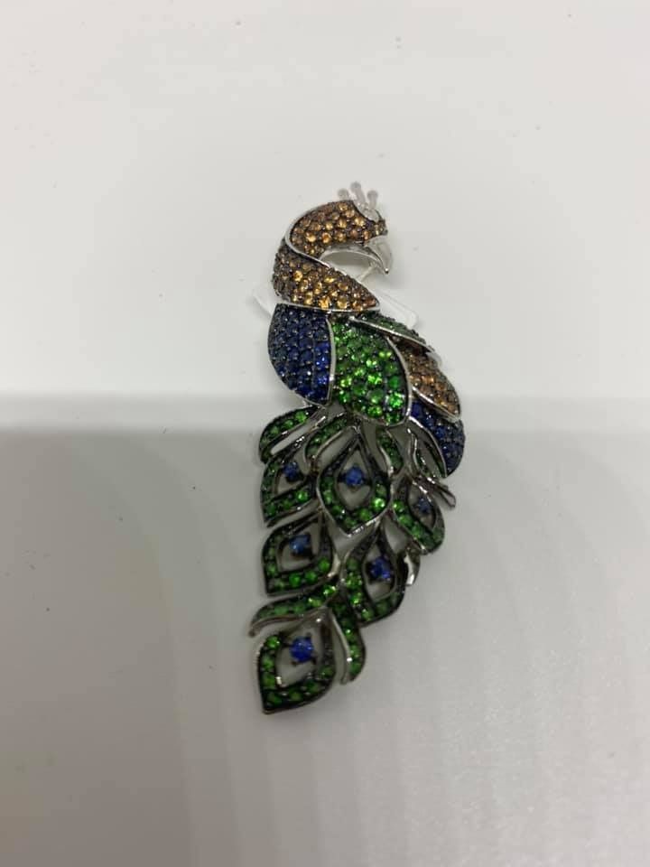 Colorful jeweled peacock brooch with blue, green, and gold stones on a white background