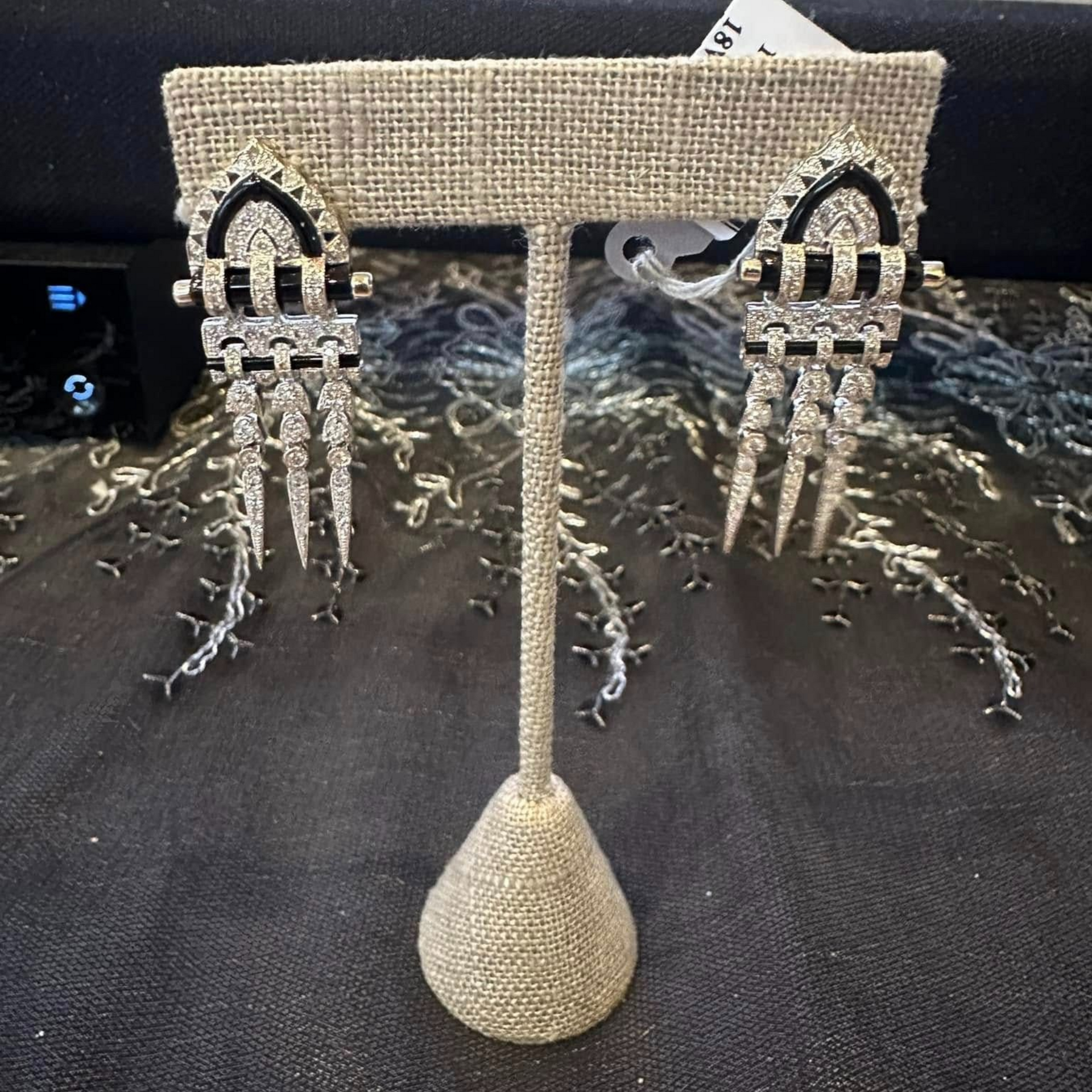 Beaded necklace display stand with two dangling black-and-clear beaded earrings on a tabletop.