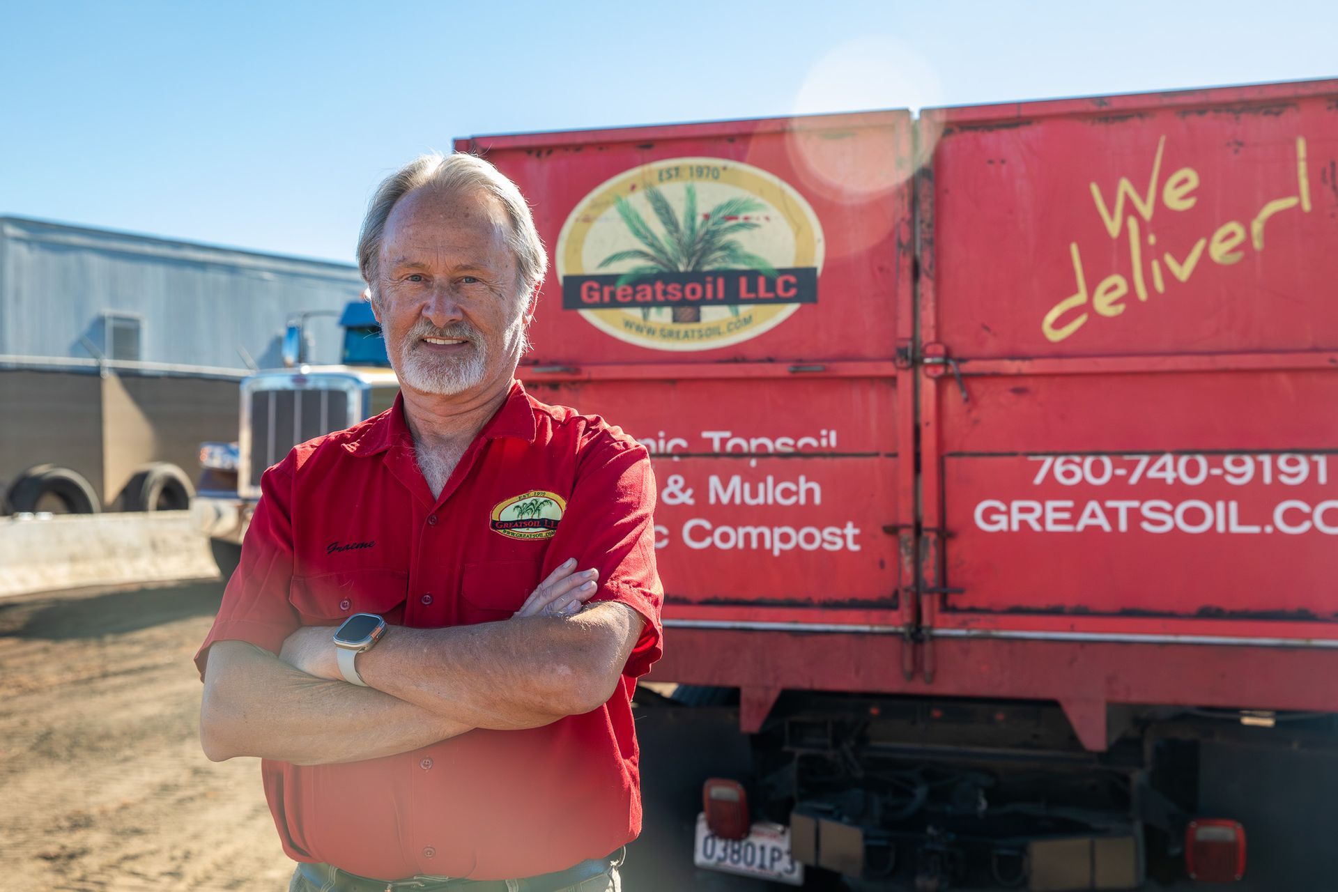 Man in red shirt stands with arms crossed in front of a red truck with company logo.