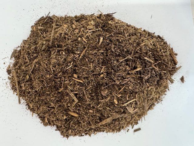 Pile of dark brown mulch on a white surface, consisting of shredded wood pieces and soil.