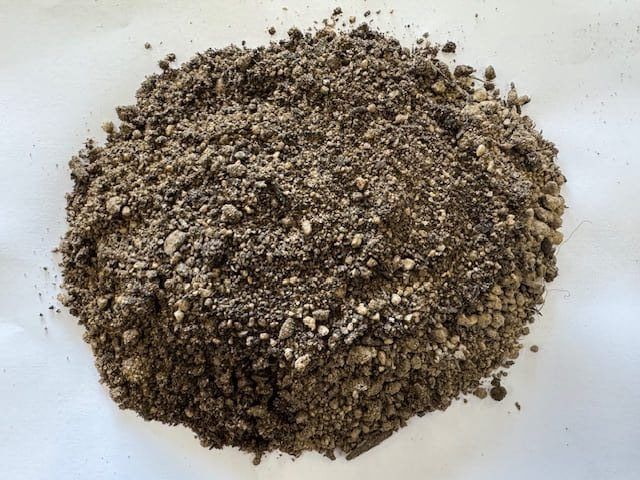 Pile of dark brown soil with small white and gray particles.