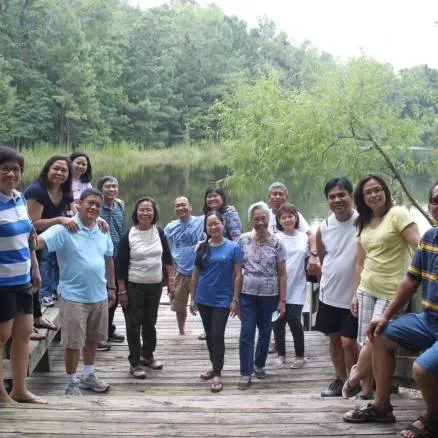 Group of people posing on a wooden dock by a lake, surrounded by trees.