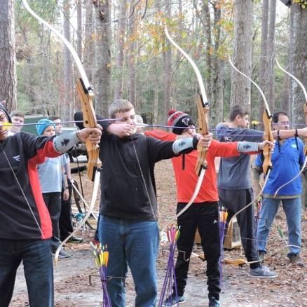 People in a forest archery range aiming bows at a target.