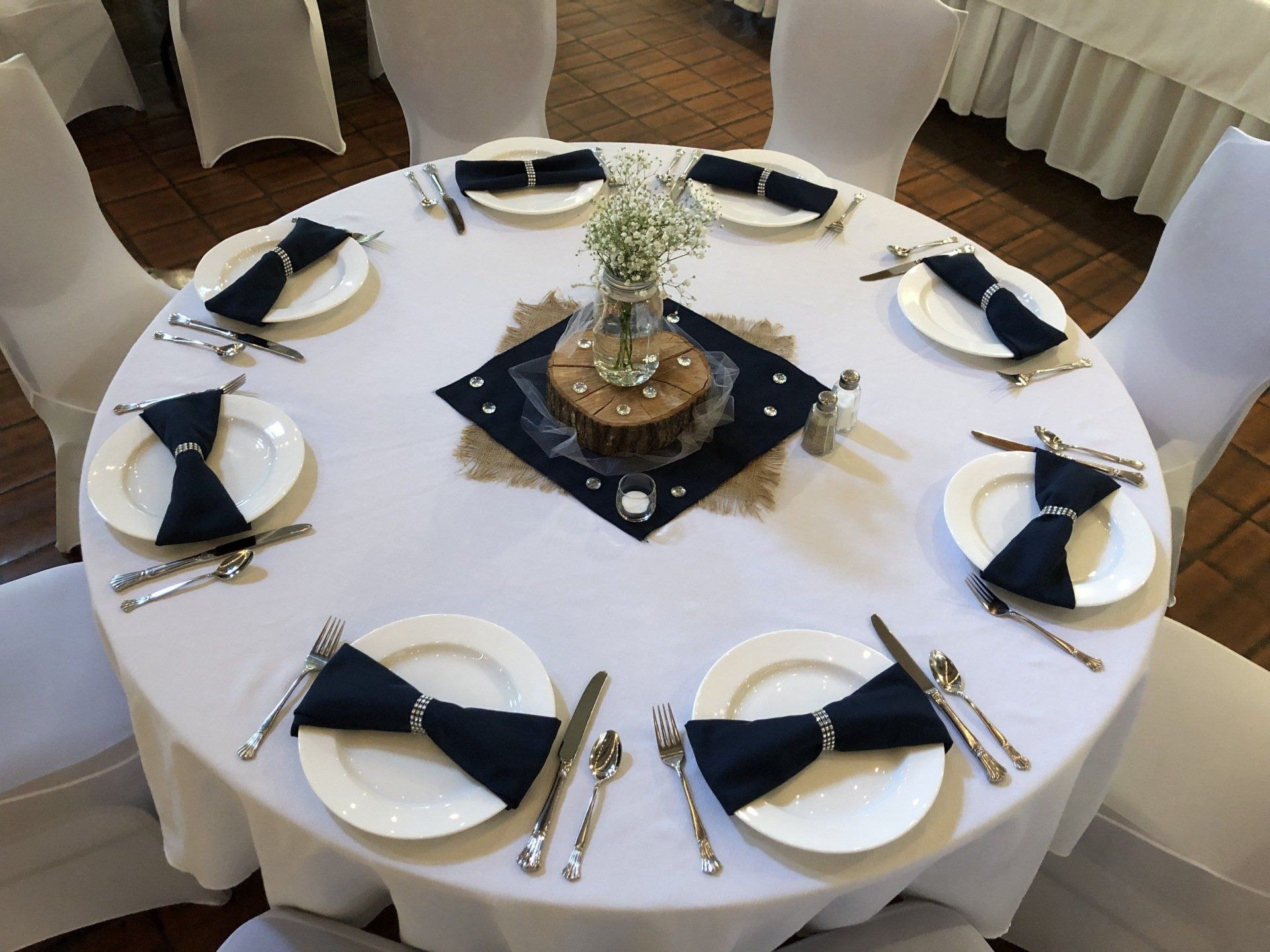 Round table set for a formal event with white tablecloth and navy napkins with silverware.