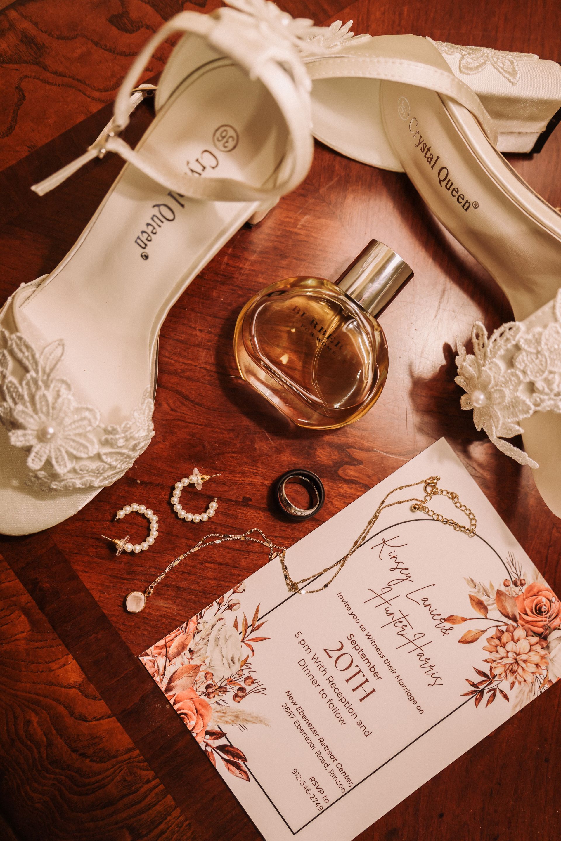 Wedding details: white shoes, perfume, jewelry, invitation on a wood surface.