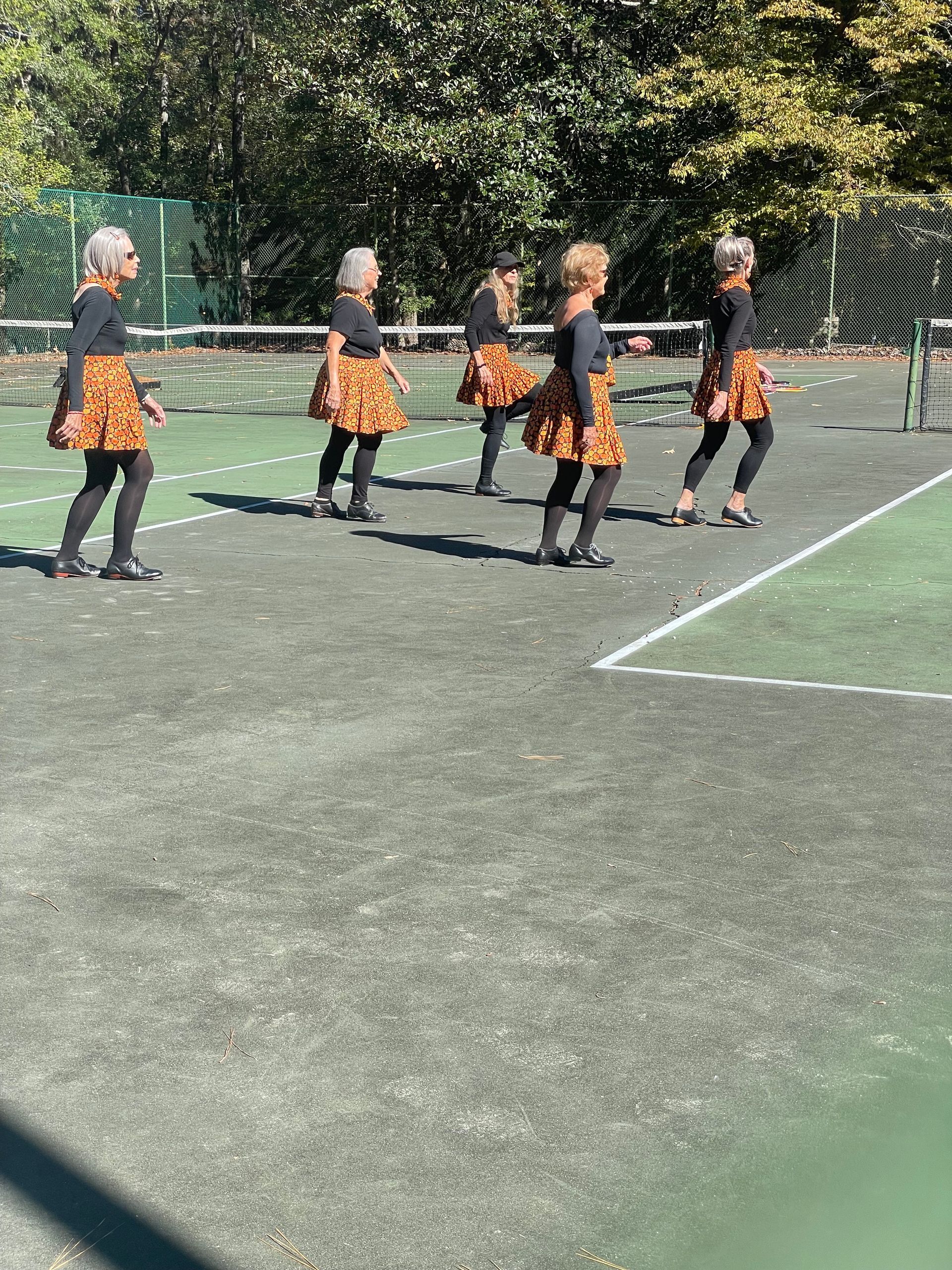 Five people in matching skirts and black tops dance on a court.