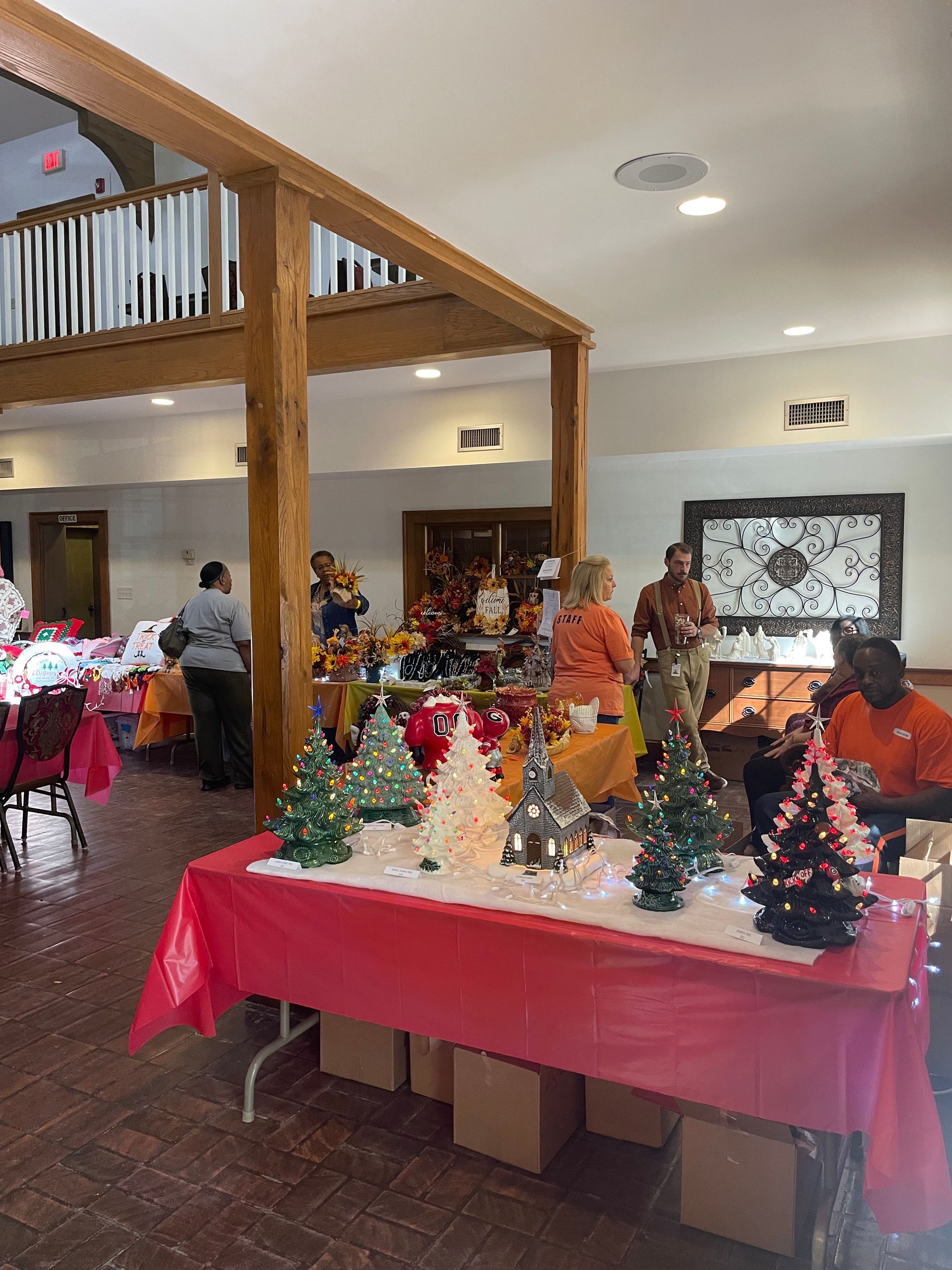 Holiday event with decorated tables. People mingle near festive Christmas trees and ornaments.