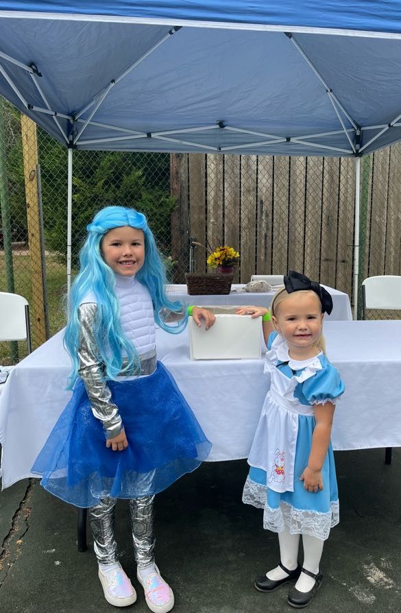 Two children in Alice in Wonderland costumes posing under a tent.