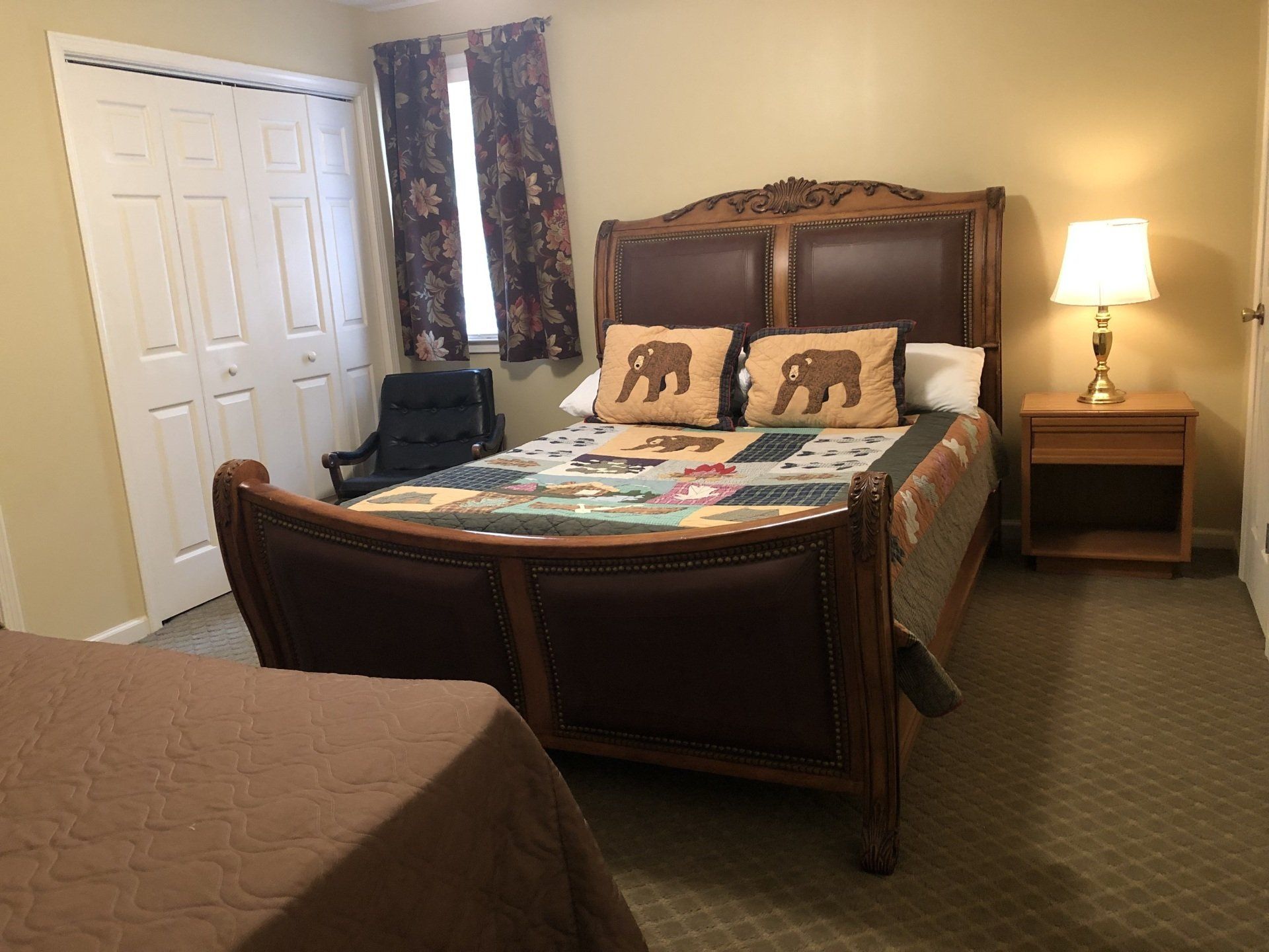Bedroom with a large ornate bed, a smaller bed in the foreground, and a nightstand with a lamp.