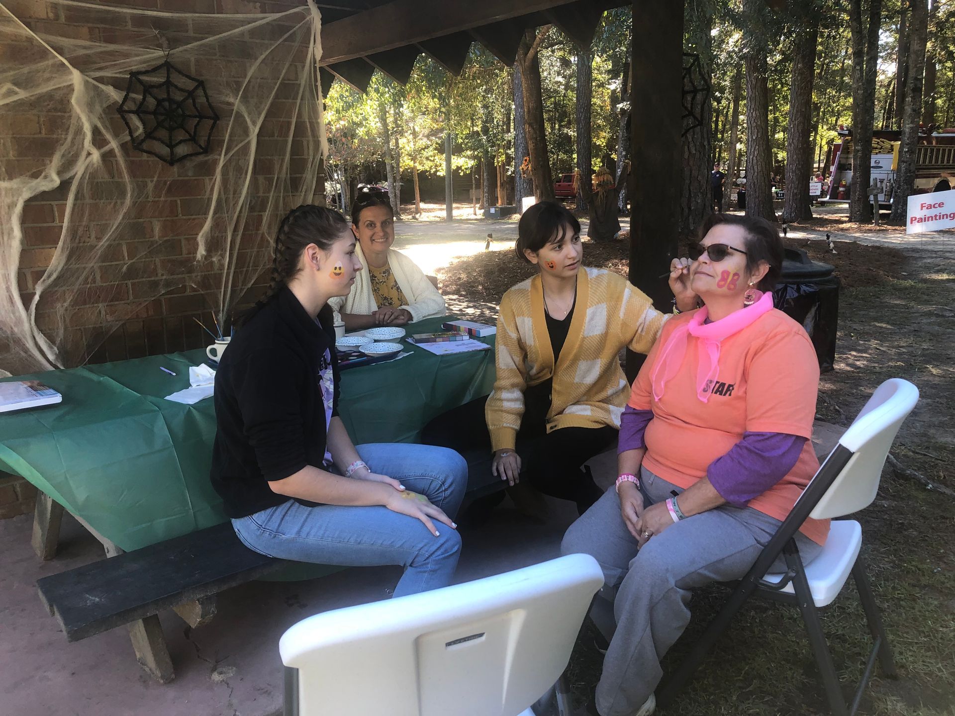 People getting face paint at an outdoor event under a decorated shelter.