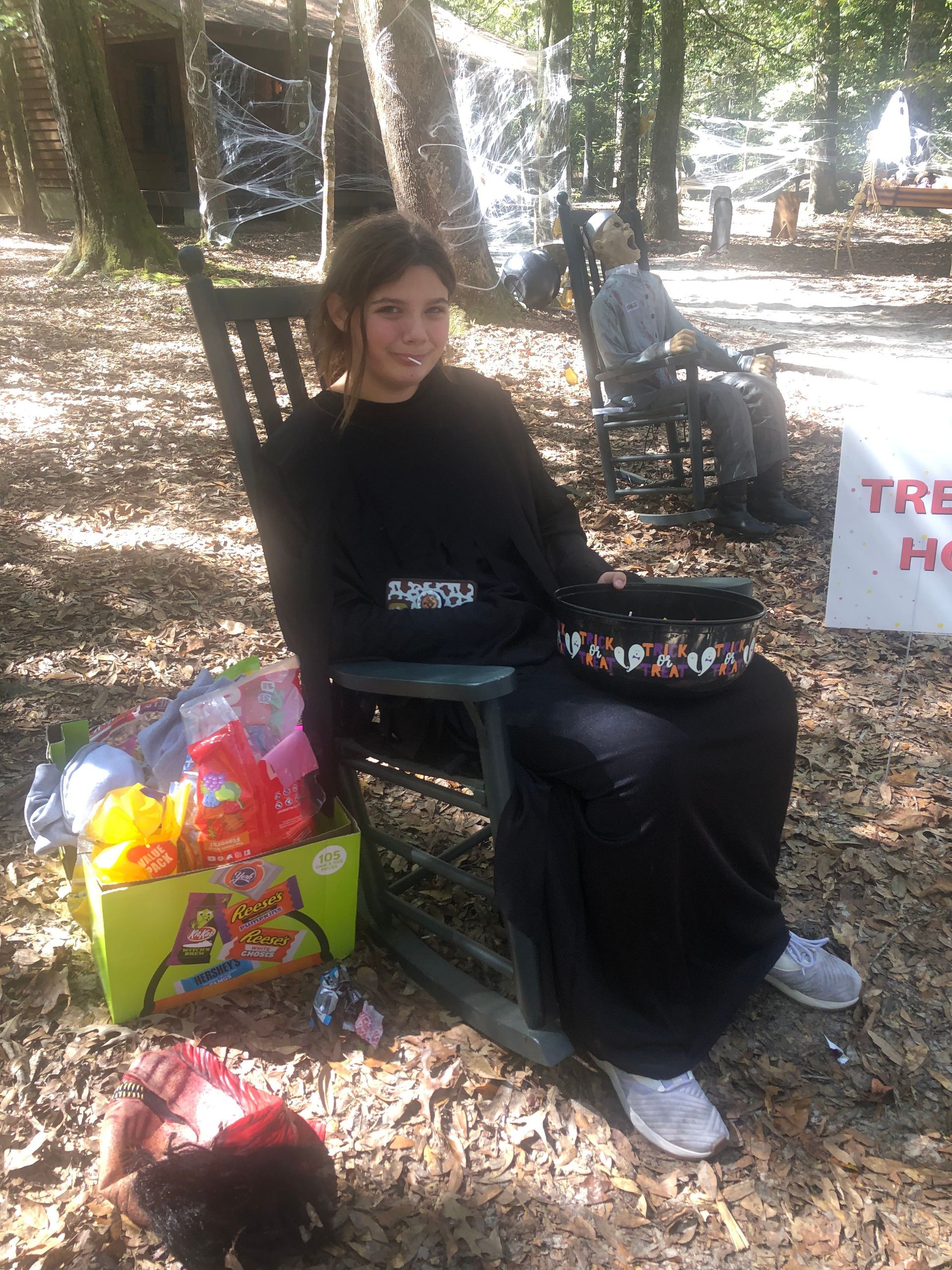 Person sitting in a rocking chair outdoors, near a box of toys. Another person is in the background.