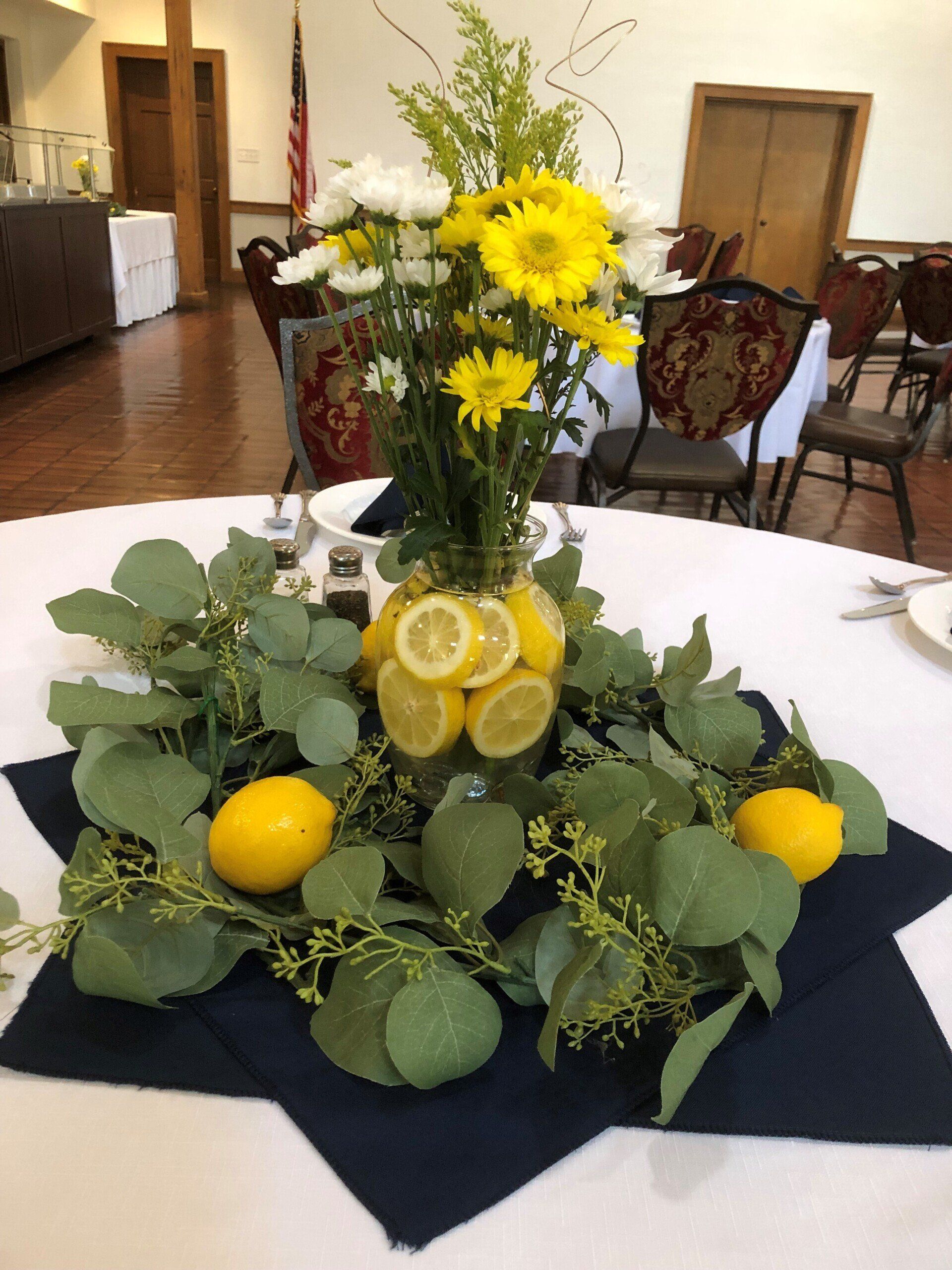 Centerpiece with lemons, flowers, and greenery on a table set for an event.