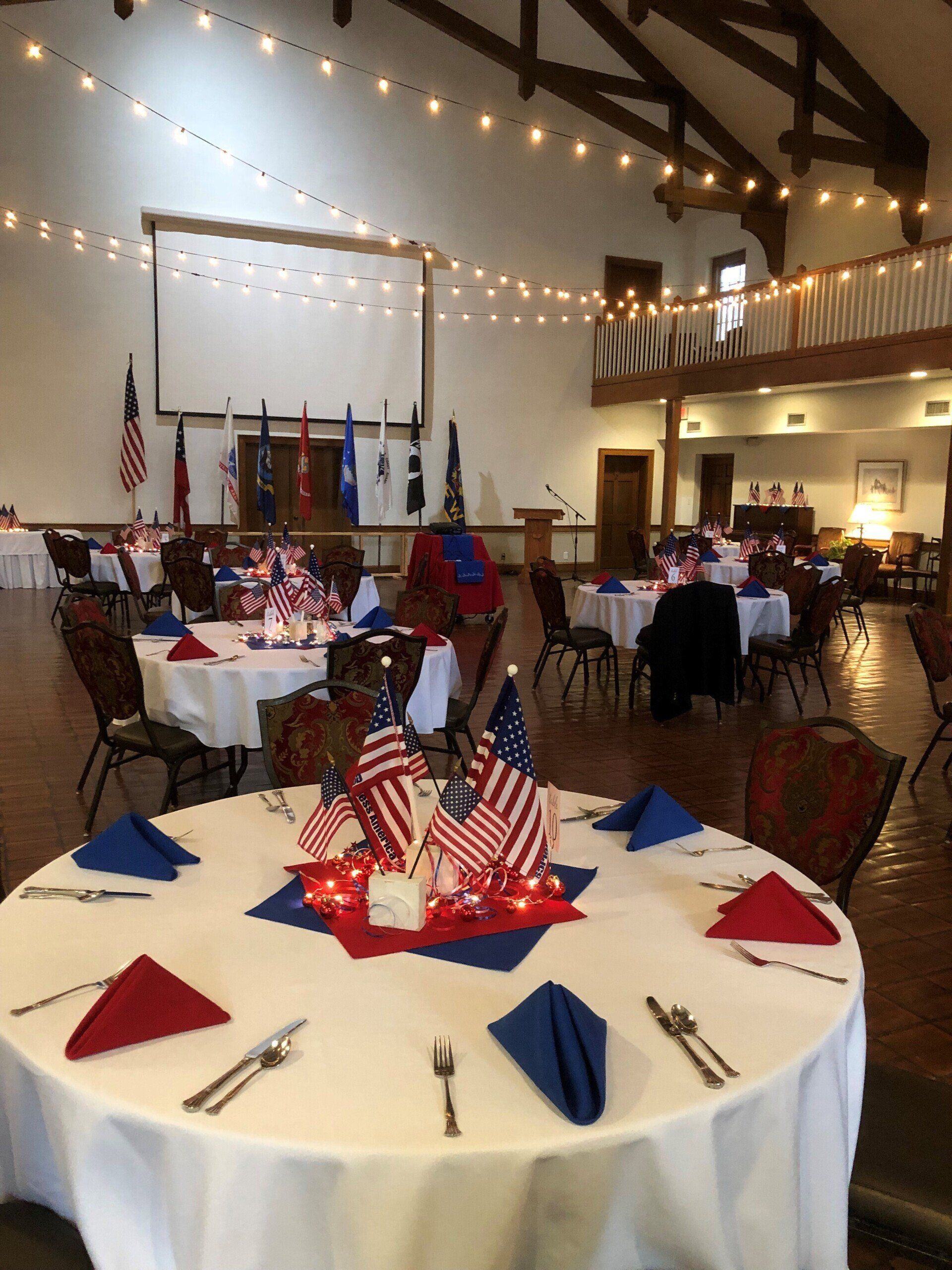 Banquet hall decorated in red, white, and blue for a patriotic event. Tables set with flags and decorations.