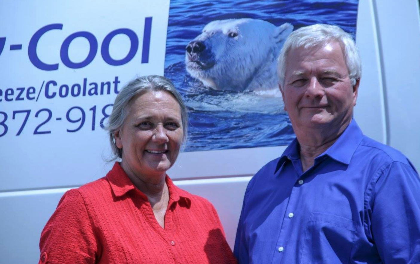 Two people stand next to a van with a polar bear graphic. Man in blue, woman in red smiling.