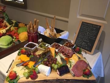 Charcuterie table with fruit, cheeses, meats, breadsticks, and a small chalkboard menu display