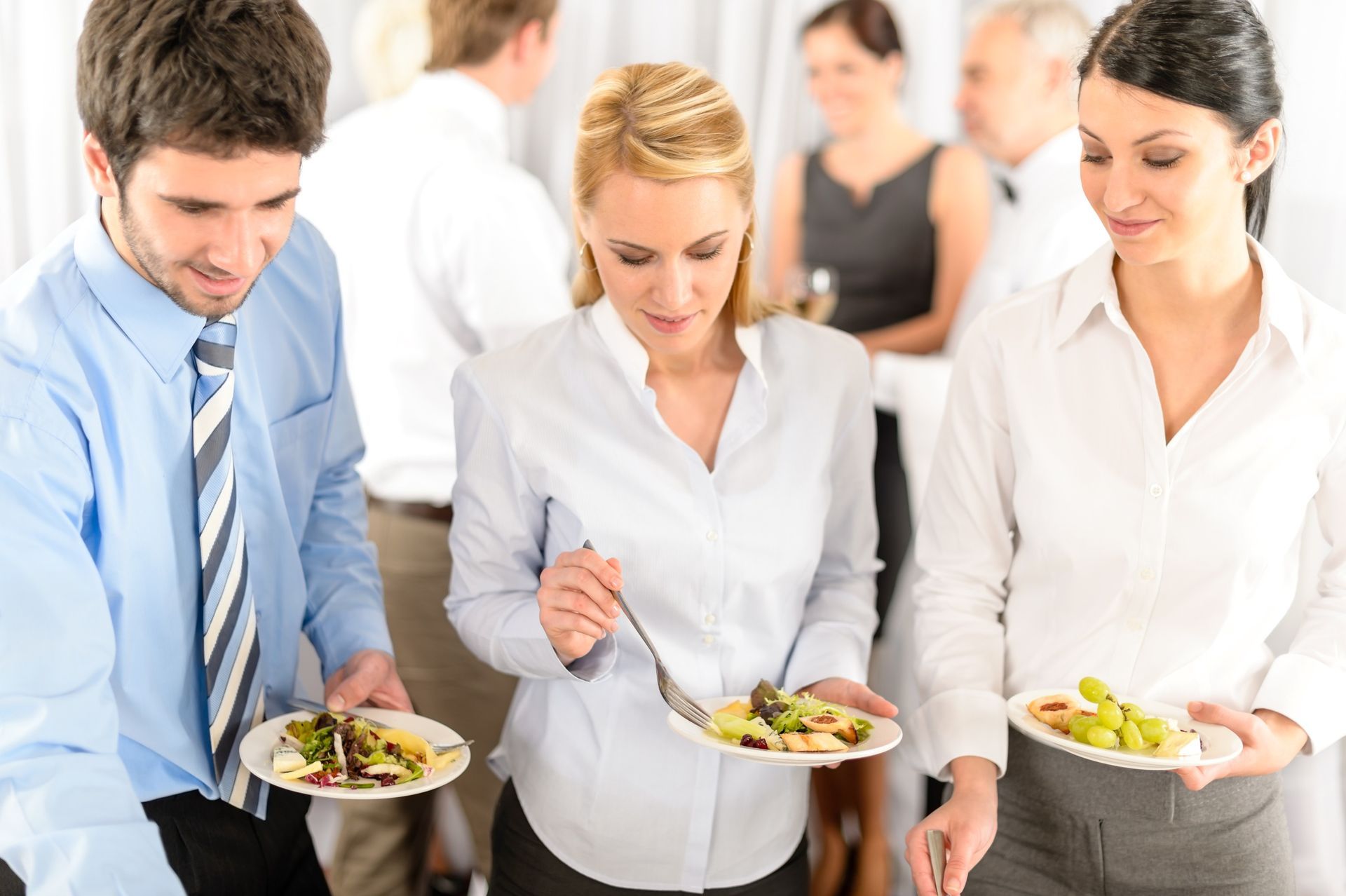 People at a buffet, holding plates of salad and talking in a bright office setting