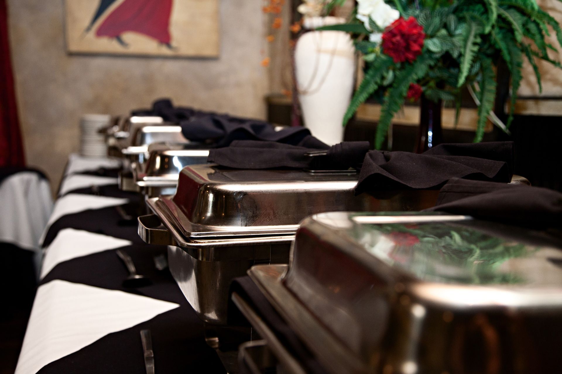 Row of covered chafing dishes on a banquet table with black napkins, set for a catered event