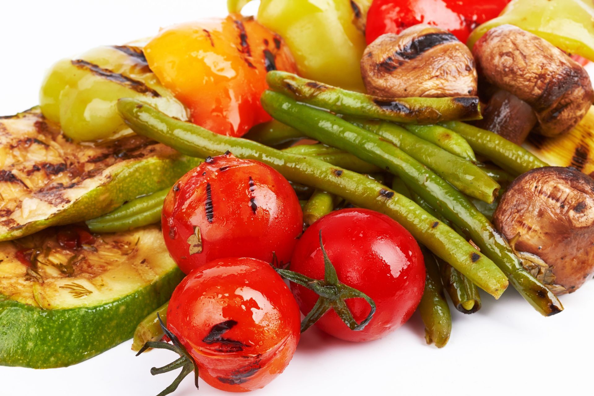 Grilled vegetables and cherry tomatoes on a white plate, with green beans, peppers, zucchini, and mushrooms