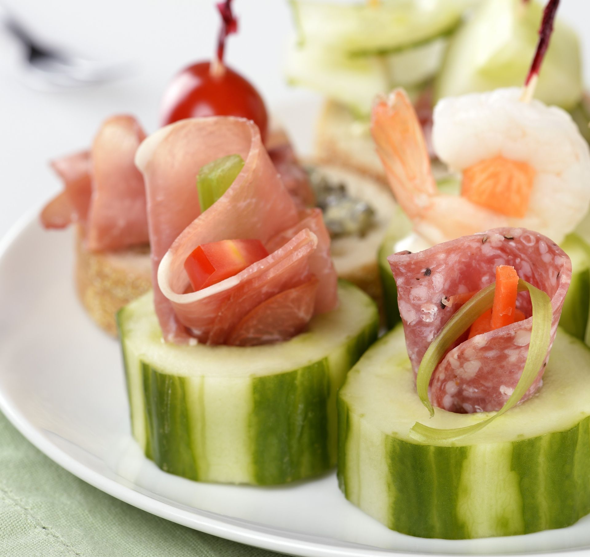 Cucumber appetizer bites topped with cured meat and shrimp on a white plate