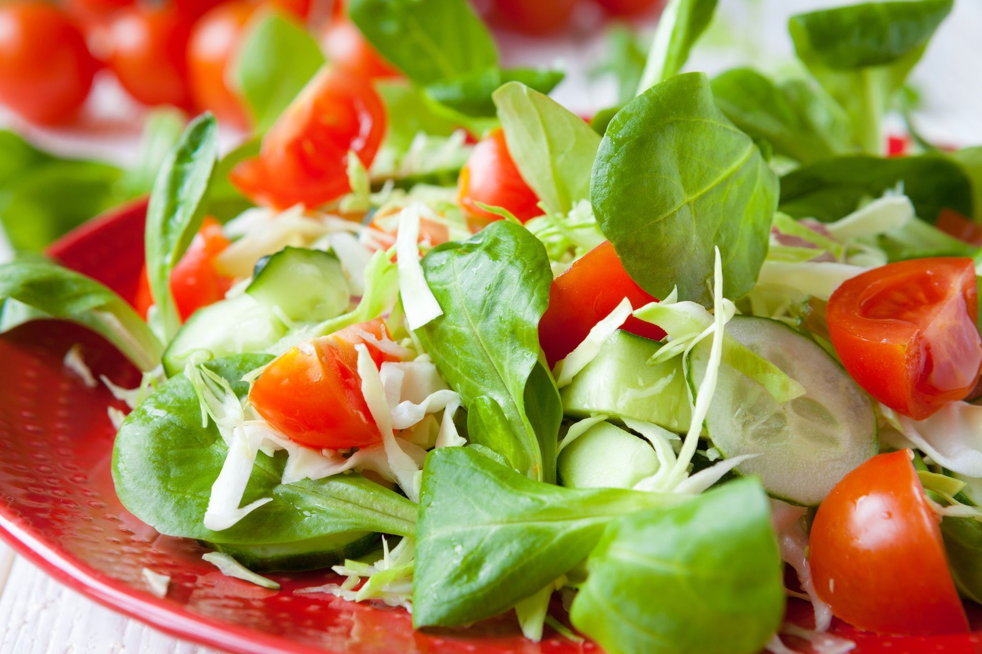 Fresh green salad with lettuce, tomatoes, cucumber, and shredded cheese in a red bowl