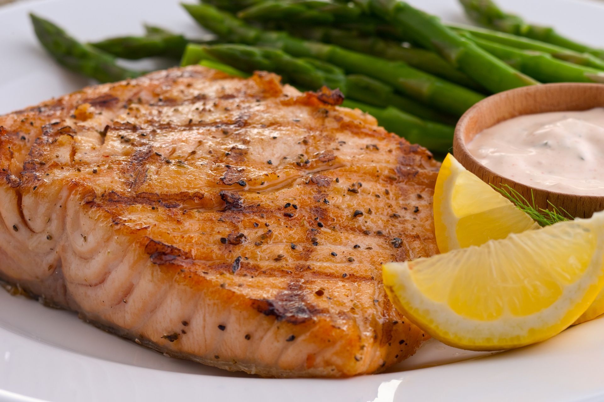Grilled salmon fillet with asparagus, lemon wedges, and dipping sauce on a white plate