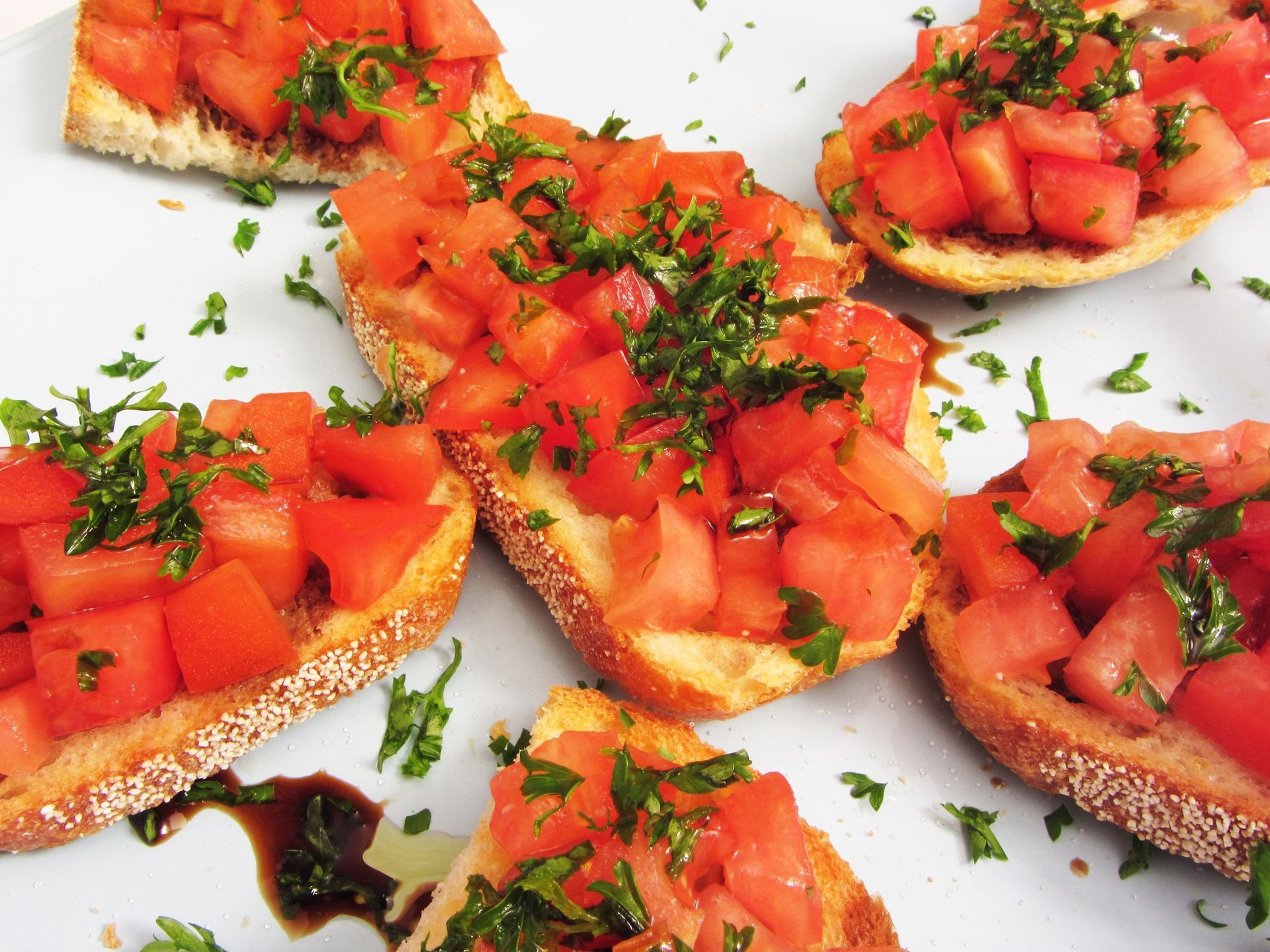 Bruschetta slices topped with diced tomatoes and chopped herbs on a white plate