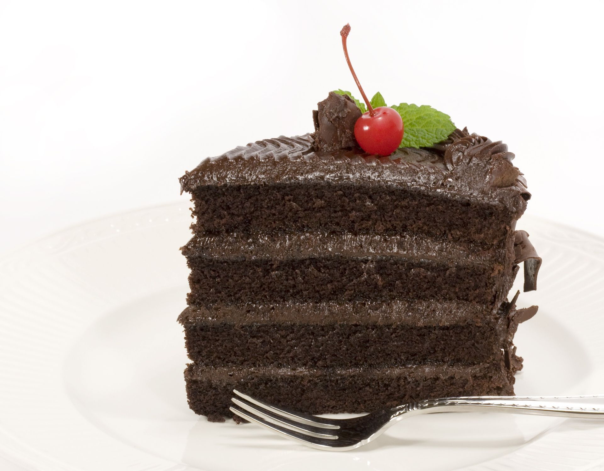 Chocolate layer cake slice topped with a cherry and mint leaf on a white plate with a fork