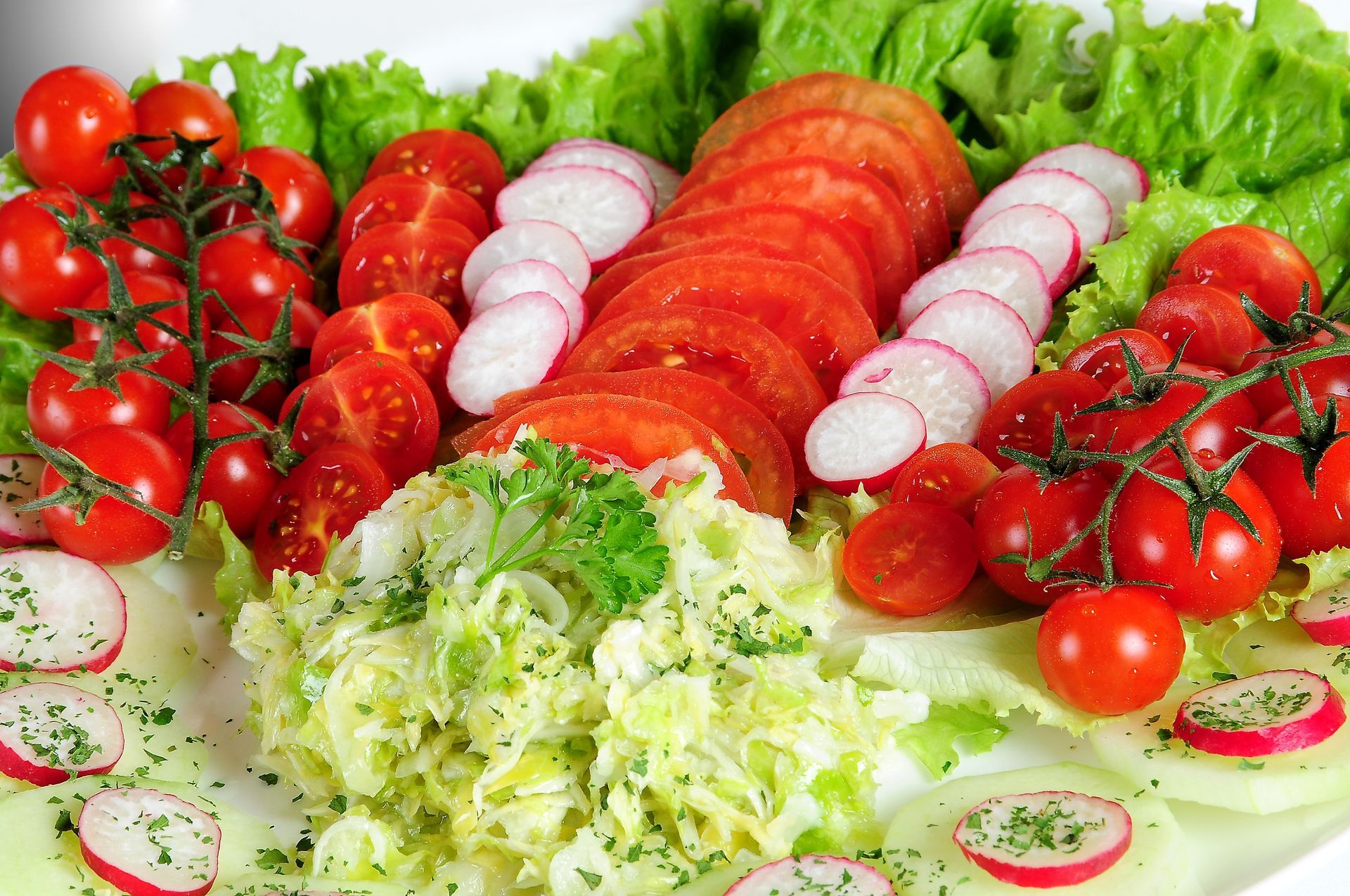 Fresh salad platter with tomatoes, radishes, lettuce, and cucumber slices arranged on a white plate