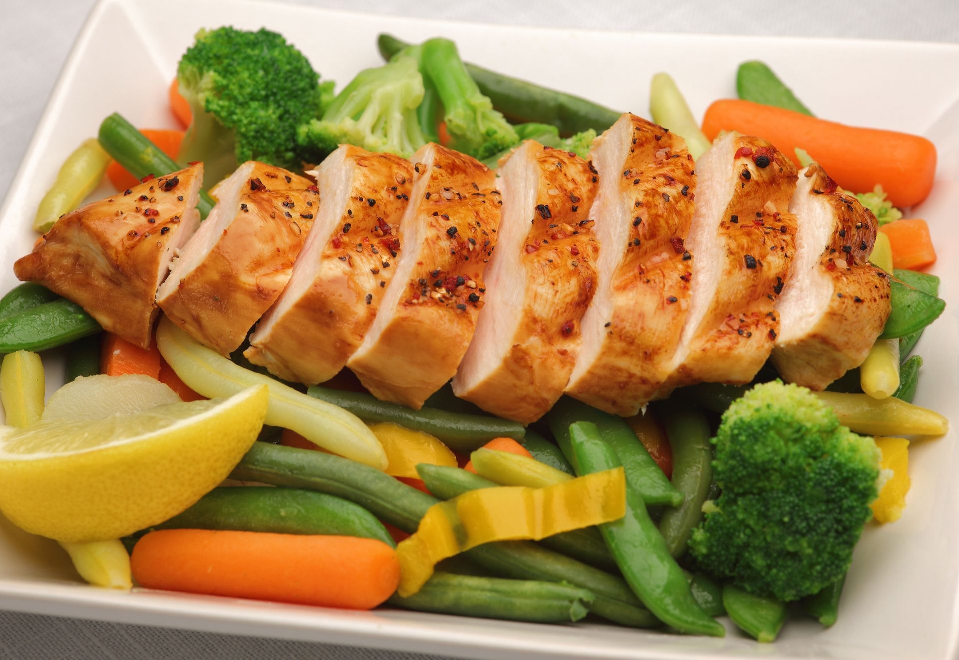 Grilled chicken breast with lemon wedges and mixed vegetables on a white platter